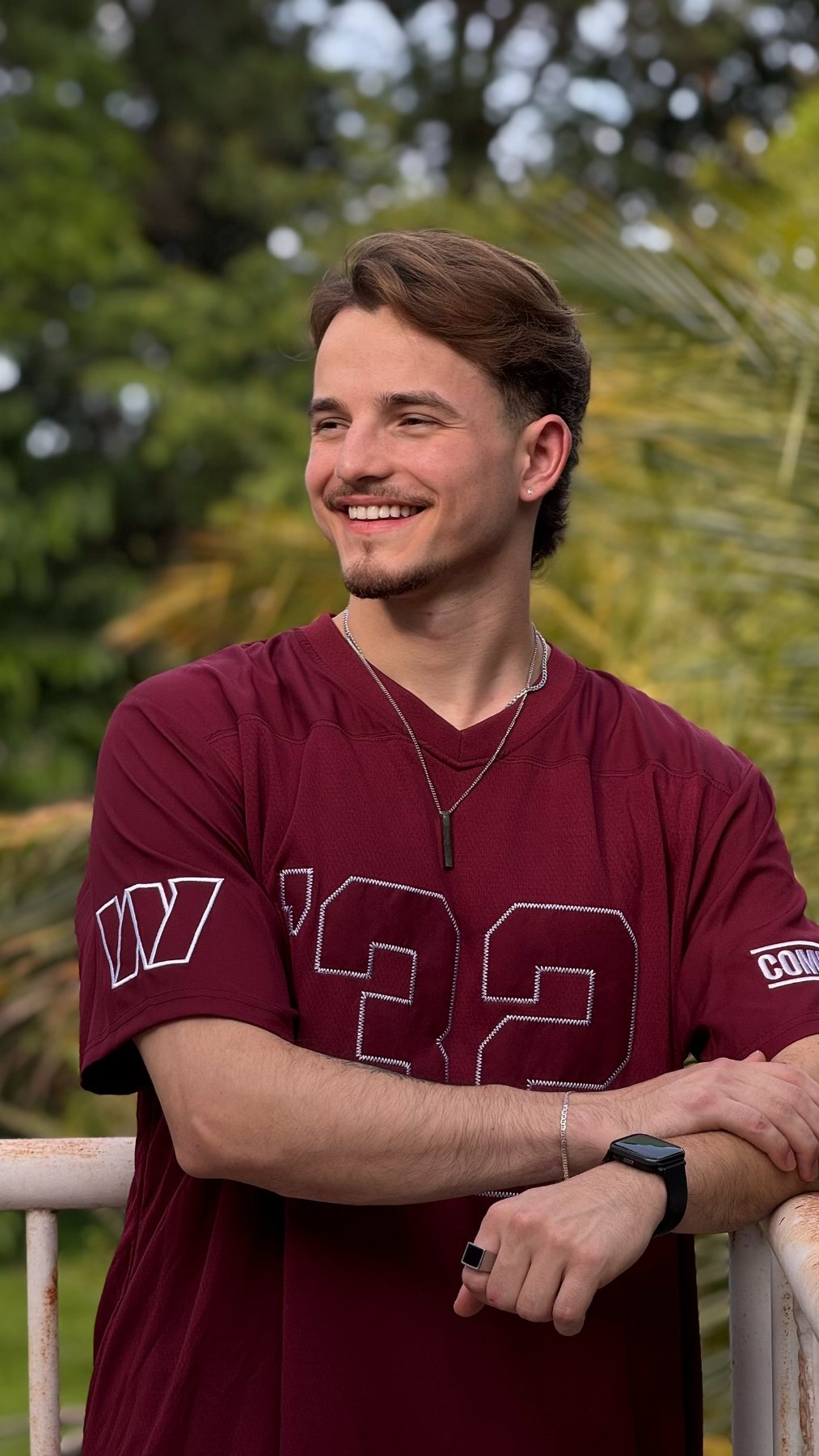 Igor sorrindo ao ar livre, com camiseta vinho